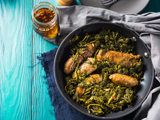 Italian sausages with rapini broccoli in a skillet with table setting on green wooden table