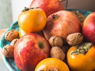 Naklejka na ściany i meble Autumn fresh fruit food persimmons, pomegranate, apples, nuts, in the kitchen on a dish