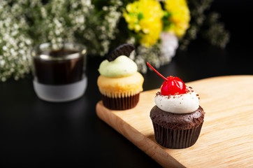 Cup cakes chocolate and sweet cherry with cream cheese and a cup of black coffee, isolated black background.