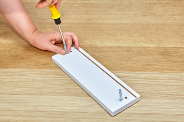 Furniture assembler tightens connector bolts into furniture with screwdriver.