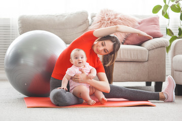 Young pretty mother working out with her little child at home