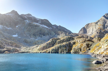 The lower Blue Lake (Ibon Azul), among barren rocky mountains with snow and a blue sky in a sunny...