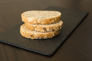 Slices of homemade multigrain bread on black slate board