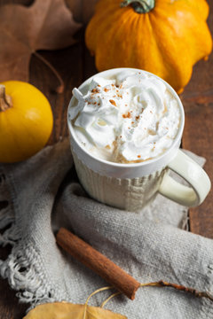 Spicy pumpkin latte with cinnamon and autumn leaves on wooden background