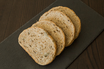 Slices of homemade multigrain bread on black slate board