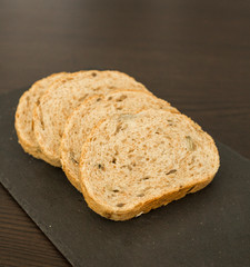 Slices of homemade multigrain bread on black slate board
