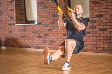 Strong muscular man exercising with trx facilities in gym or workout center