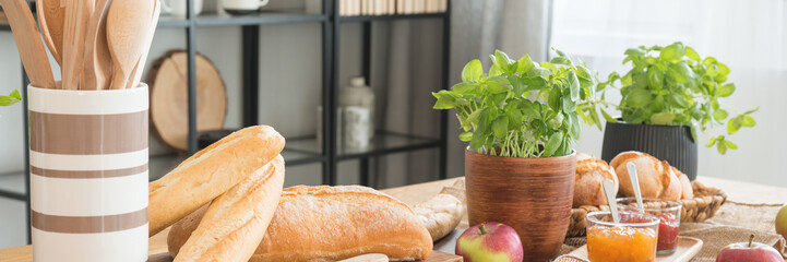 Panorama on basil and baguettes on table with apples and jam in dining room interior. Real photo