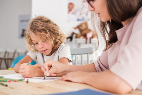 Close-up of a child with an autism spectrum disorder and the therapist by a table drawing with crayons during a sensory integration session.