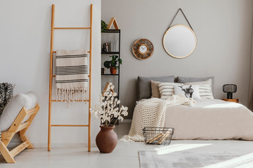 Scandi open space bedroom interior with double bed with knit blanket and many pillows, rack with books and decor, carpet on the floor in real photo - Powered by Adobe