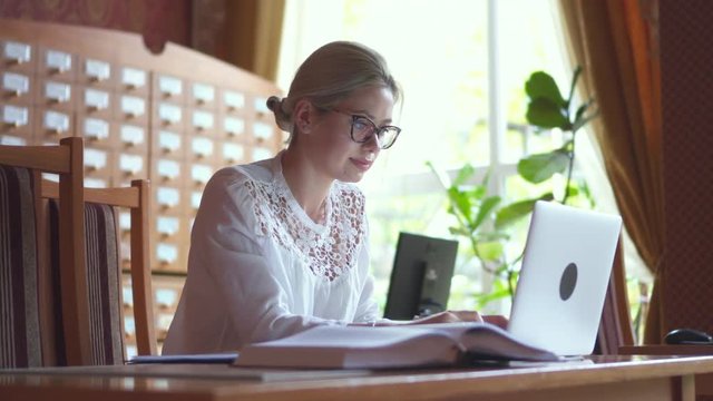 Woman using laptop and looking at textbook in library
