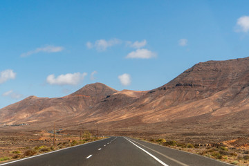 Empty straight road leading towards the mountains as seen trough the windscreen of the car, in Lanzarote, Canary Island, Spain. Road trip concept.