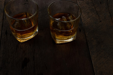 Glass of alcohol scotch whiskey with ice on wooden table and black background
