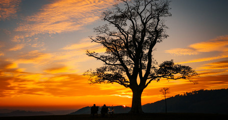 Fototapeta na wymiar Loving couple watching sunset Great Lhota under an old lonely tree on a hill beautiful orange sunset sky full of clouds...