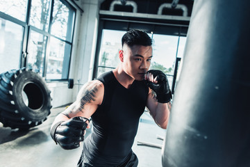 young sportsman wearing boxing gloves and punching boxing bag at gym