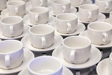 Lot of white porcelain tea pairs in piles in a straight line. Concept conference at the hotel, break, catering, breakfast