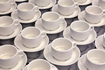 Lot of white porcelain tea pairs in piles in a straight line. Concept conference at the hotel, break, catering, breakfast