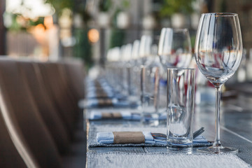 Restaurant serving and glass wine and water glasses, forks and knives on textile napkins stand in a row on a gray wooden table. Concept banquet, birthday, conference, group lunch