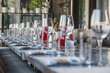 Restaurant serving, glass wine and water glasses, forks and knives on textile napkins stand in a row on a gray wooden table. Concept banquet and birthday, conference, group lunch