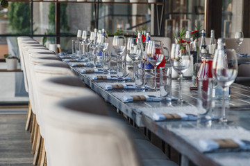 Restaurant serving, glass wine and water glasses, forks and knives on textile napkins stand in a row on a gray wooden table. Concept banquet and birthday, conference, group lunch