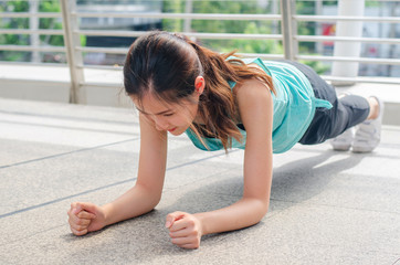 Fit girl in sportswear doing plank exercise outdoor in the street city warm summer day. Concept of endurance and motivation.