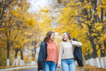 Young pretty girls having fun outdoors in autumn background. Cheerful friends in the fall time