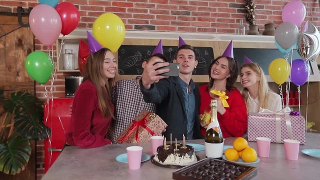 Cheerful friends taking selfie at the birthday party, good-looking young people celebrating important event after work in spacious flat