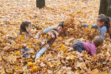 Children are lying and playing on fallen leaves in autumn city park.