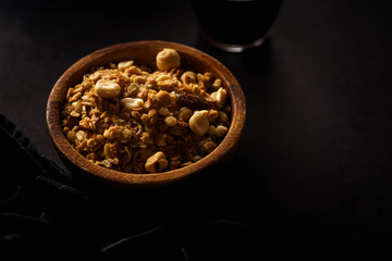 Obraz na płótnie Canvas Roasted granola with nuts in wooden bowl with a cup of coffee on black table.