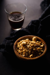 Roasted granola with nuts in wooden bowl with a cup of coffee on black table.