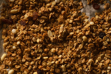 Top view of roasted granola with nuts, flakes and raisins on parchment paper. Close up texture