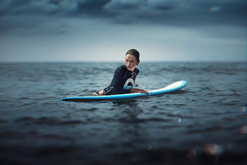 girl with surf board wait big ocean wave,dramatic sky and toning. lifestyle, people water sport lessons and beach swimming activity on summer vacation