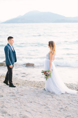 Young bride woman in beautiful blue wedding dress walking to the groom on the beach near the Garda lake. Wedding day and love concept.