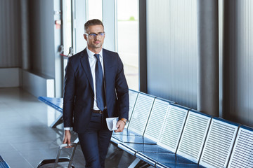 adult handsome businessman in glasses with baggage and tickets walking at airport