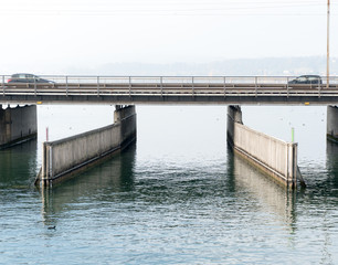 concrete bridge over water with a train line and road running parallel and a boat and ship passageway below and two cars heading toward each other