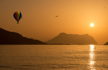 Aerostatic balloon at sunrise in the sea next to an island