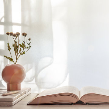 An open book and a vase with flowers on a wooden table lit by the sun. Copy space
