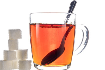 Transparent mug with tea on a white background next to the pieces of sugar and oatmeal cookies