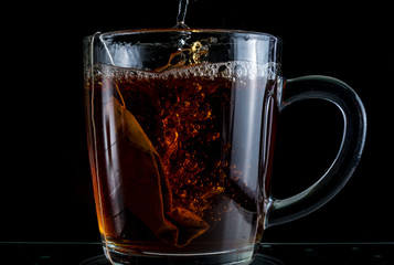 Brewing a tea bag in a transparent mug with sugar on a black background, a storm in a glass