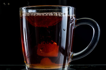 Brewing a tea bag in a transparent mug with sugar on a black background, a storm in a glass
