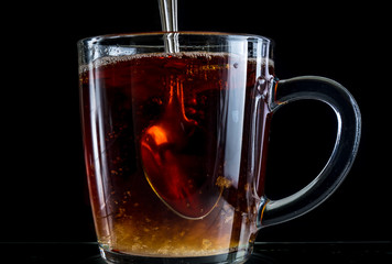 Brewing a tea bag in a transparent mug with sugar on a black background, a storm in a glass
