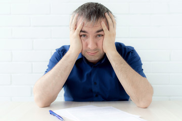 Thinking businessman touching his head holding a document sitting at the table.a man in business...