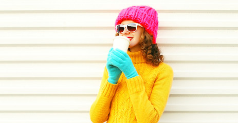 Cool girl drinks coffee from cup wearing knitted colorful pink hat yellow sweater over white background