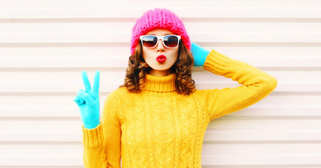 Cooll funny girl blowing red lips wearing colorful knitted yellow sweater pink hat in gloves over...