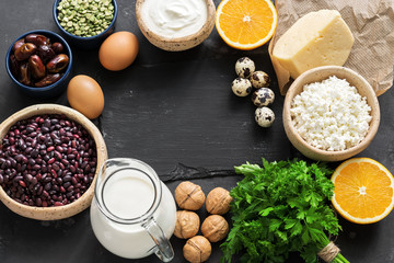 Foods high in calcium on a dark stone background. Healthy eating concept. Dairy products, legumes, greens, eggs and fruits. Top view, place for text.