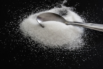 heap of sugar with a teaspoon on black background