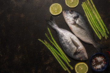 Fresh dorado fish with asparagus and spices, ingredients for cooking on a dark background. Top view, place for text, flat lay.