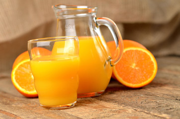 Naklejka na ściany i meble Glass full of orange juice, carafe with fresh juice and fresh oranges in the background on wooden table