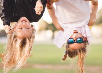 Two young girls, age 8-12, hanging upside down on outdoor fitness device
