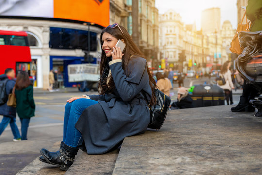 Junge, attraktive, webliche Touristin in London sitzt am Picadilly Circus und telefoniert mit ihrem Handy